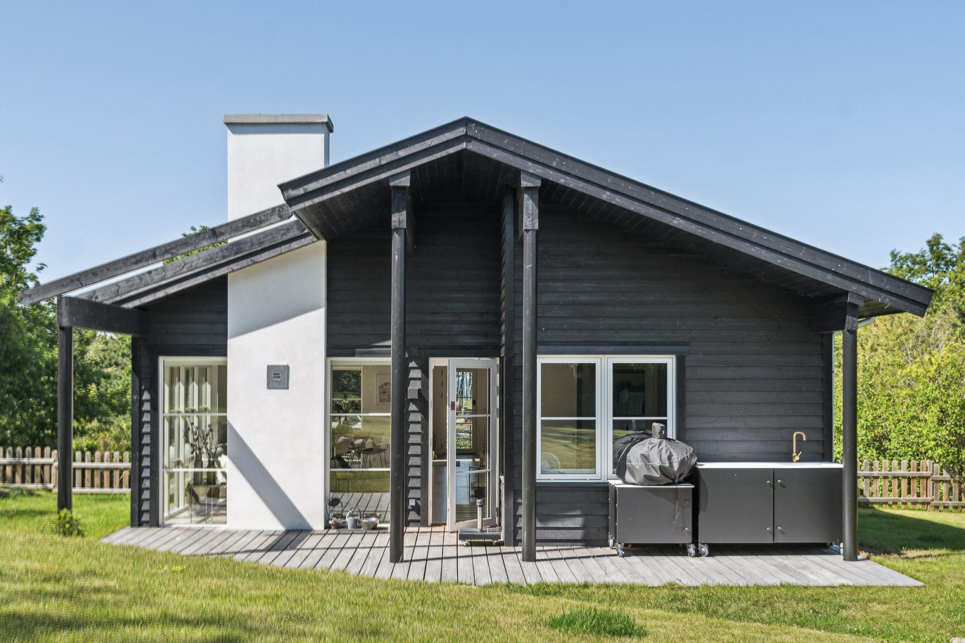 Husets gavl med overdækket terrasse, udekøkken og hvid skorsten