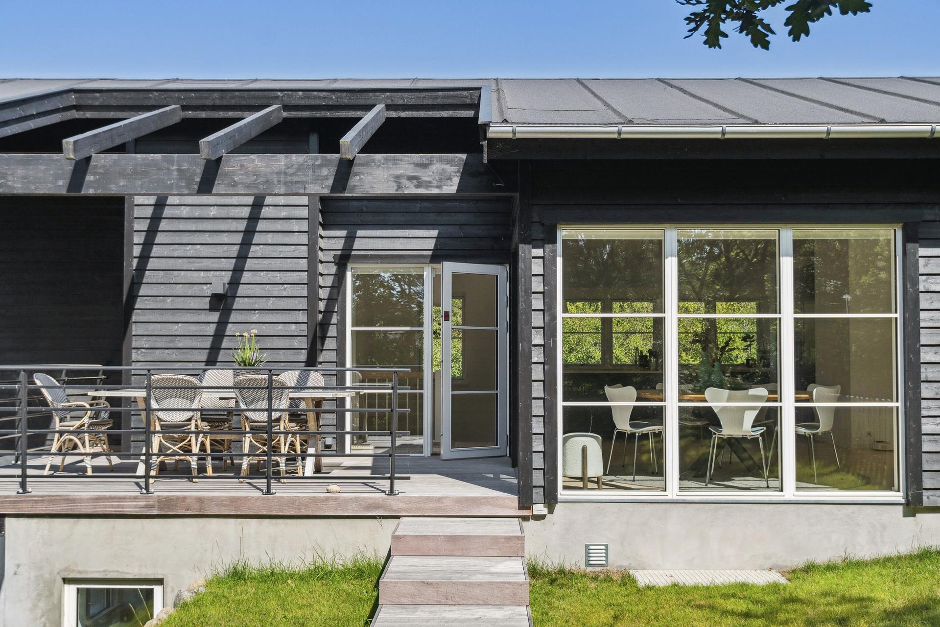 Hævet træterrasse med spisebord langs husets sortmalede facade